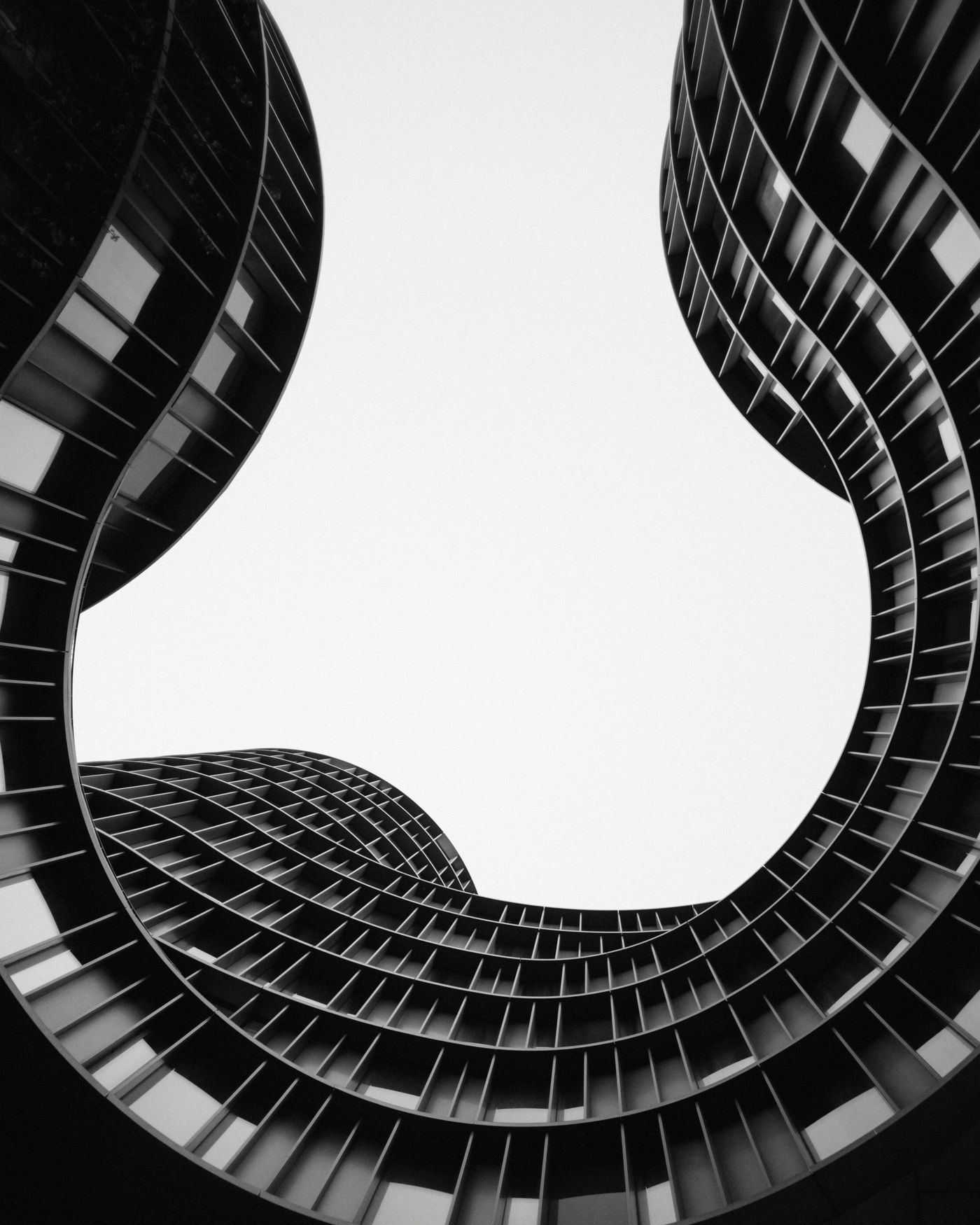 Vue en contre-plongée d'un immeuble à l'architecture courbe, photographie noir et blanc.